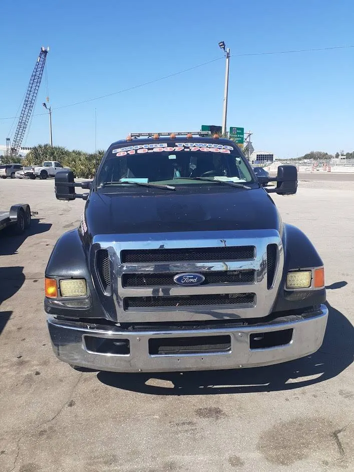 Front of the black Empire Towing Ford truck in a sunlit lot with a crane