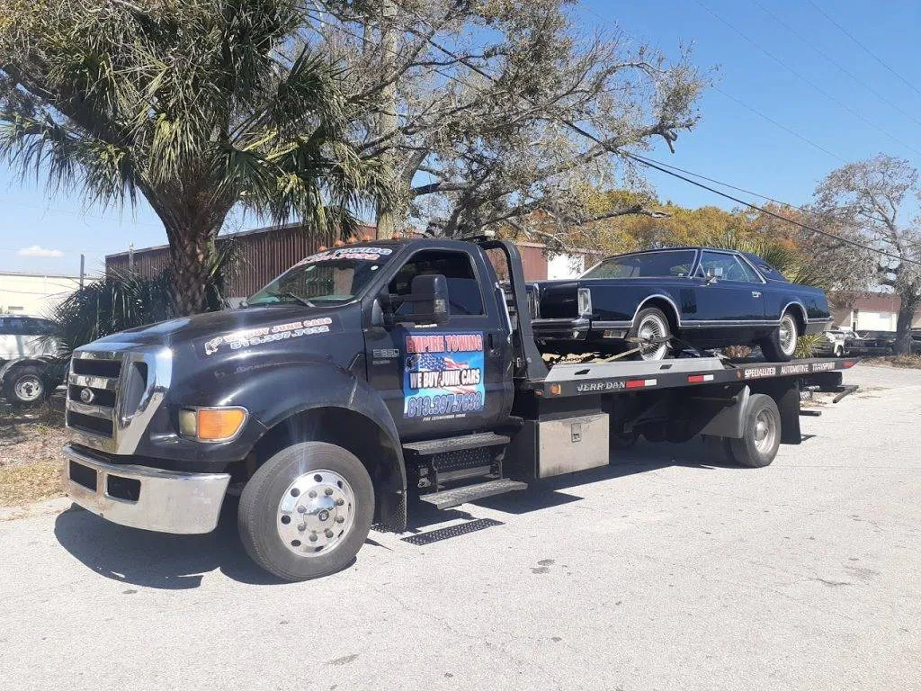 Parked in a sunny lot, the Empire Towing flatbed holds a black classic car