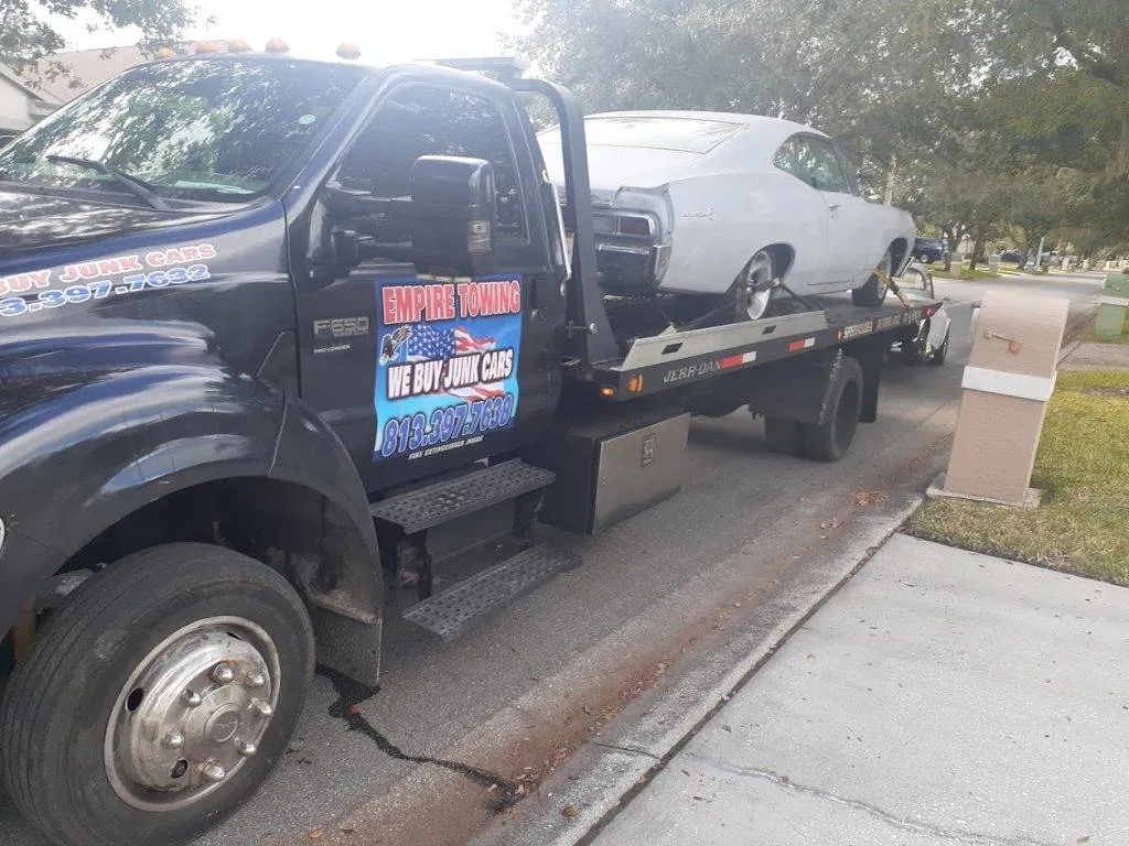 Empire Towing flatbed hauling a white classic coupe down a residential street